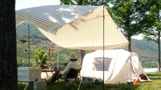 Person resting under the shade of a tarp installed on green grass