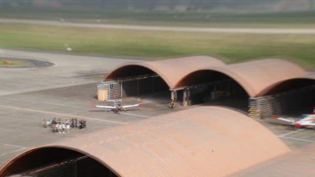 Aircraft taxiing on airport runway near hangars