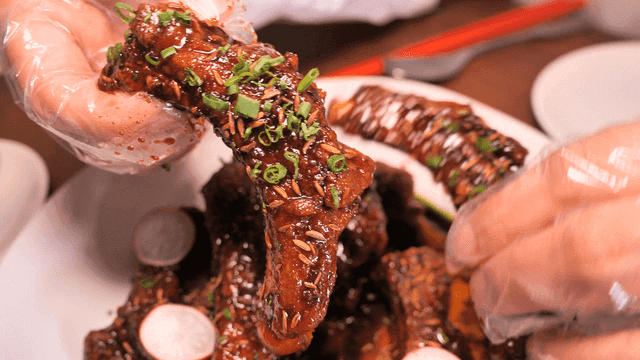 Hand holding glazed marinated short rib garnished with herbs