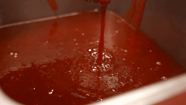 Ladle stirring red sauce in metal container