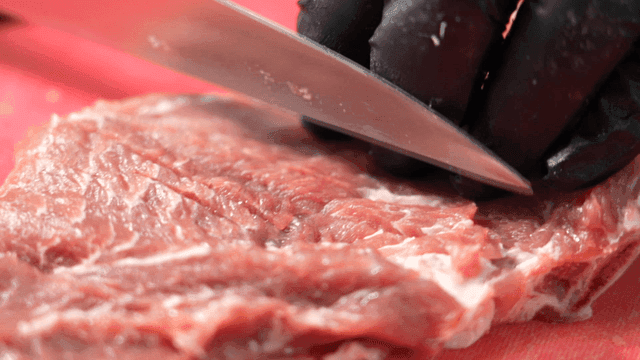 Hands making cuts in raw meat on cutting board