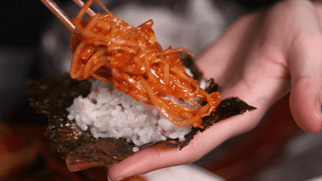 Hands placing rice and spicy bean sprouts on seaweed