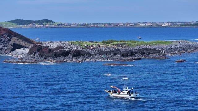 Scenic coastal view of rocky cape and boat passing nearby at sea