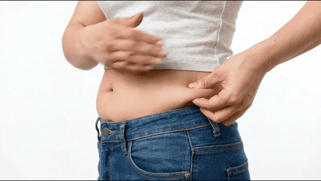 Person pinching belly fat in jeans