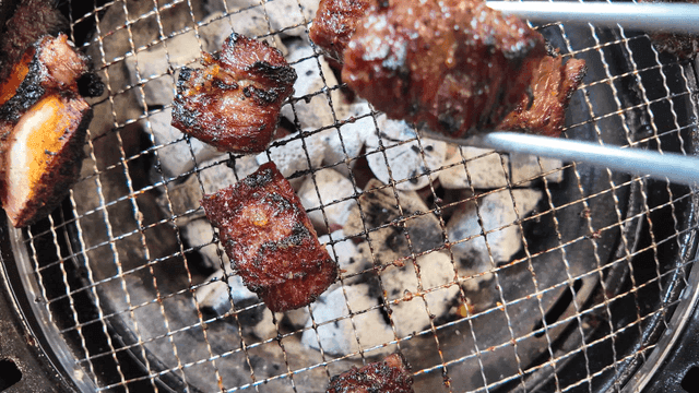 Chopsticks picking up marinated beef ribs grilling on hot plate