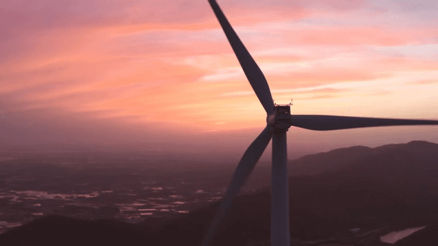 Wind turbines in a mountainous area under a pink-tinted sky