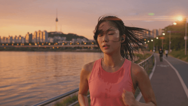 Woman jogging along riverbank at sunset