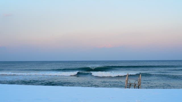 Sea waves crashing on a snowy beach under a setting sun