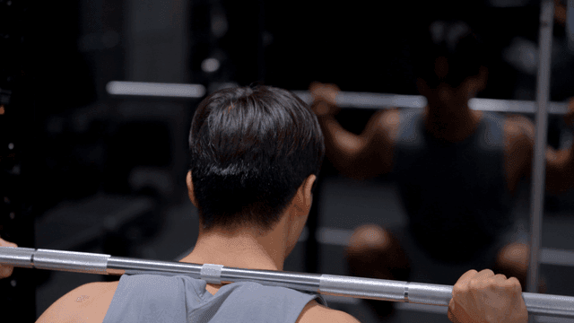 헬스장에서 어깨에 무게를 지고 스쿼트를 하는 남자