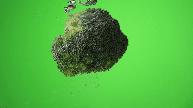 Broccoli falling into water creating bubbles on green background