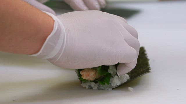 Gloved hand rolling out gimbap with crab meat salad and lettuce on a cutting board