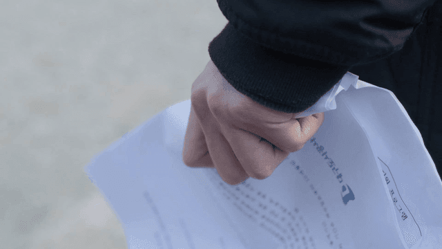 A hand holding a crumpled paper outdoors