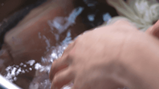 Hands dipping meat in water in large pot