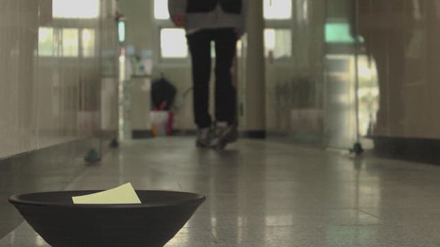 복도를 걸어와 그릇에 담긴 쪽지를 들어올리는 사람