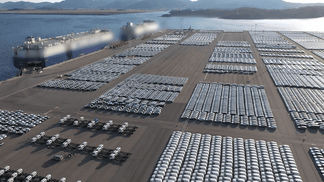 Large cargo ships and parked cars at a port