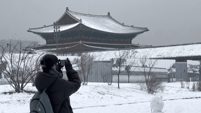 눈 내린 한국 전통 궁궐에서 사진을 찍는 여성