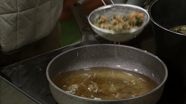 Picking freshly fried vegetables up from a frying pan with a sieve