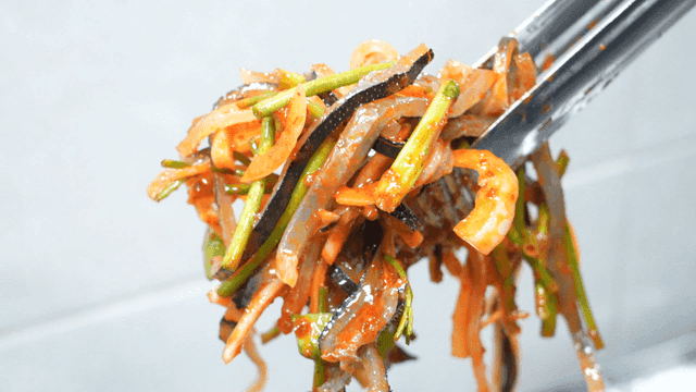 Tongs lifting seasoned pufferfish skin mixed with fresh vegetables