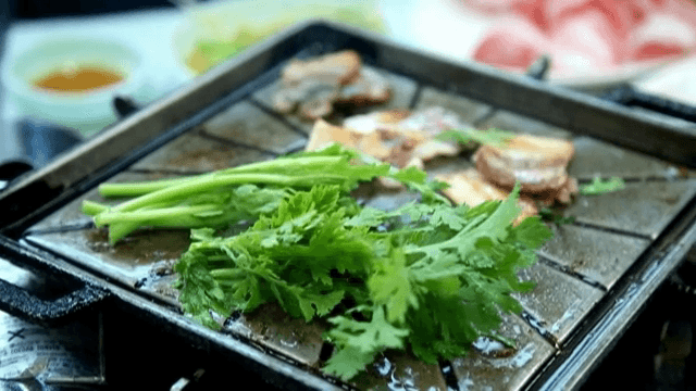 뜨거운 그릴 위에 쑥갓과 함께 삼겹살 굽기