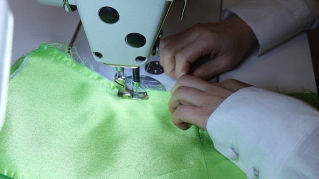 녹색 천을 재봉틀로 재봉하는 사람