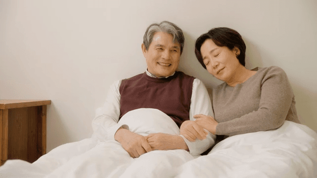 침대에 함께 앉아 있는 노부부