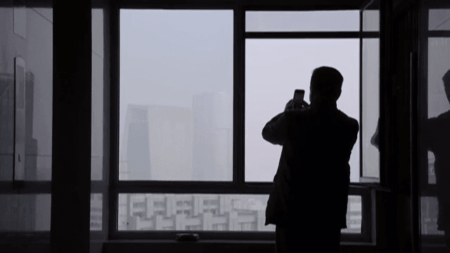 핸드폰으로 창 밖의 풍경을 찍는 남자