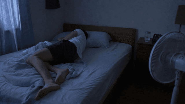 Man tossing and turning in bed in dark room