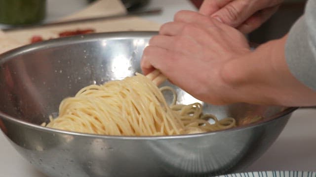 Neatly plating cooked spaghetti using chopsticks in a kitchen