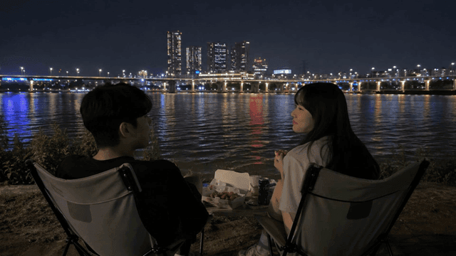 Couple eating chicken while enjoying night view by river