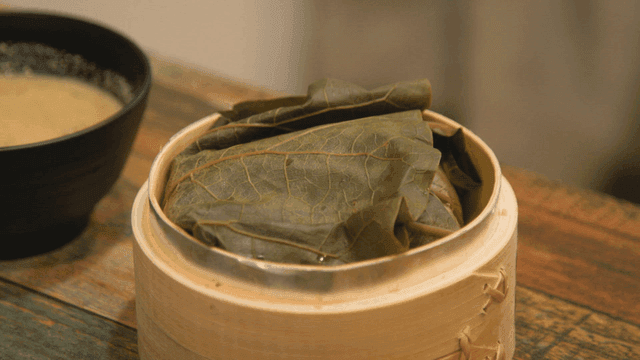 Hand opening bamboo steamer containing lotus leaf rice