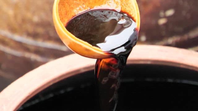 Pouring soy sauce intp a crock jar with a wooden ladle