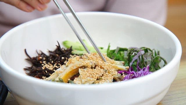 신선한 채소와 전복이 들어간 한국 비빔밥을 젓가락으로 섞는 모습