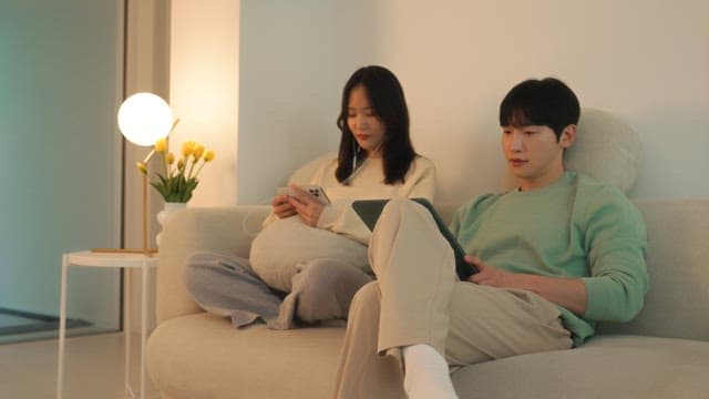 Two people using digital devices on a sofa in cozy living room