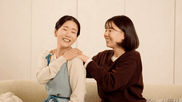 Daughter giving her mother shoulder massage on sofa.