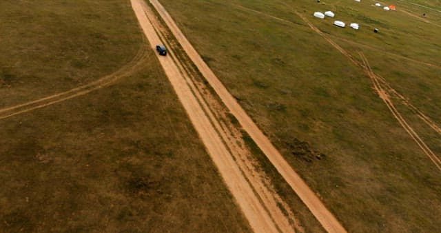 Car driving on a dirt road in open fields
