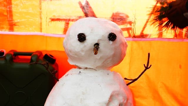 Making a snowman with pin cones and pine branchses next to an orange tent