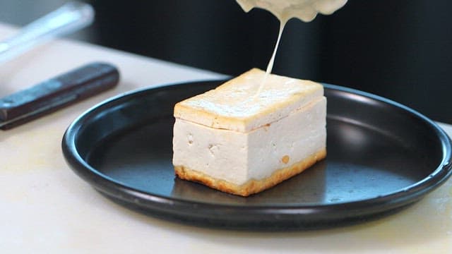 Pouring sauce over tofu on a black plate