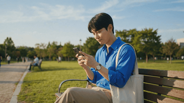 Man laughing while looking at his phone in park