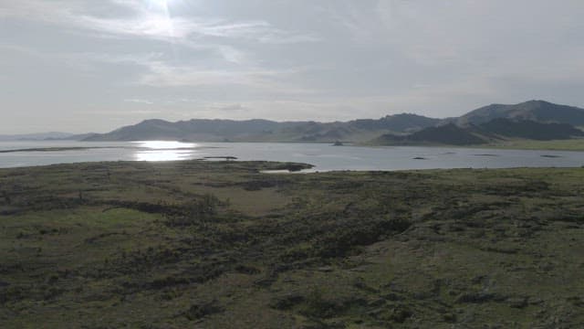 태양이 반짝이는 평화로운 호숫가와 먼 산의 전경