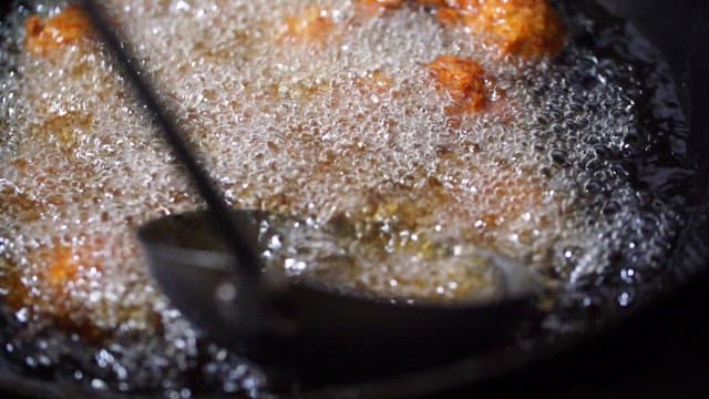 Frying meatballs in hot oil with a ladle