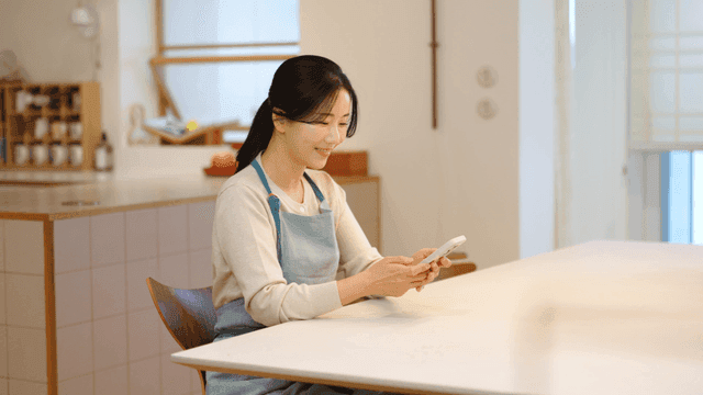 Woman wearing apron using her smartphone at home