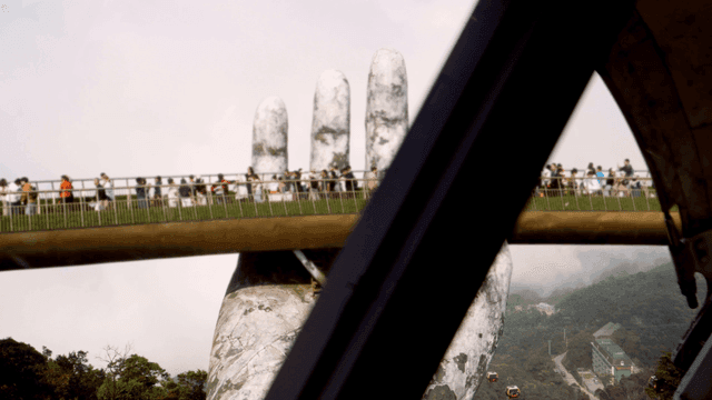 거대한 손이 받치는 다리 위의 관광객들