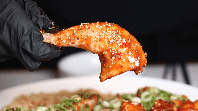 Hand lifting spicy braised chicken leg sprinkled with sesame seeds