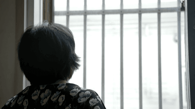 Back view of an elderly woman looking up at the sky outside the window