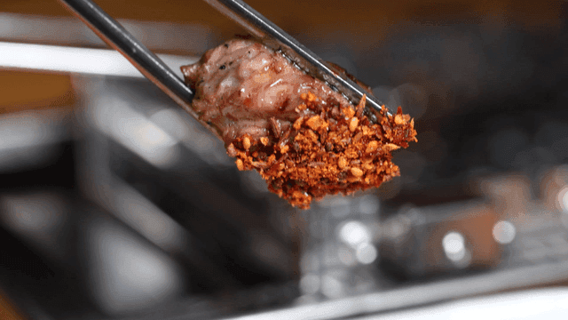 Chopsticks lifting grilled lamb skewer dipped in spicy sauce