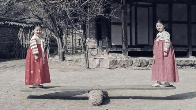 Two girls in hanbok playing on a seesaw