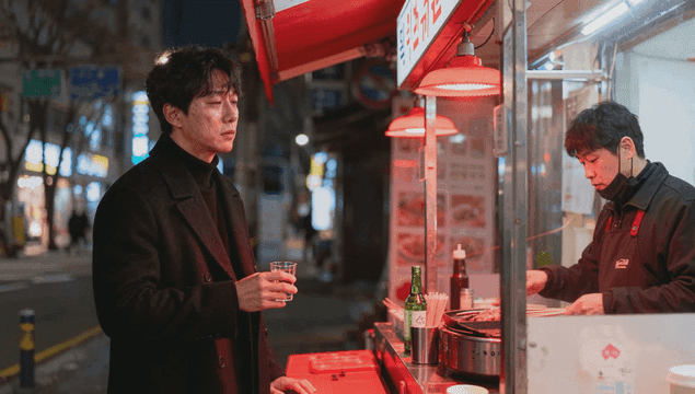 Depressed man holding a glass of alcohol and a street food stall at night