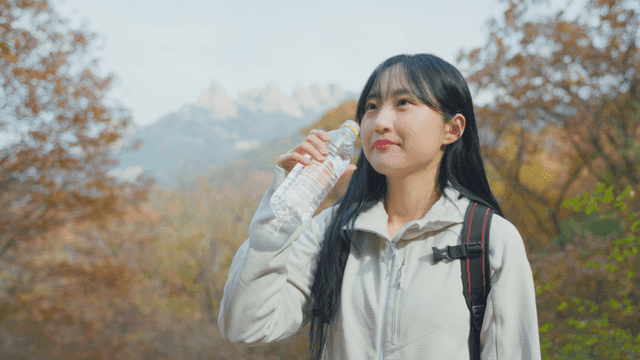 가을 산 정상에서 시원하게 물을 마시는 여성