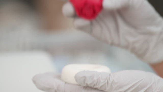 장갑 낀 손으로 베이킹 매트 위에서 장식용 꽃 모양을 만드는 모습