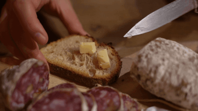 Butter being spread on bread with salami